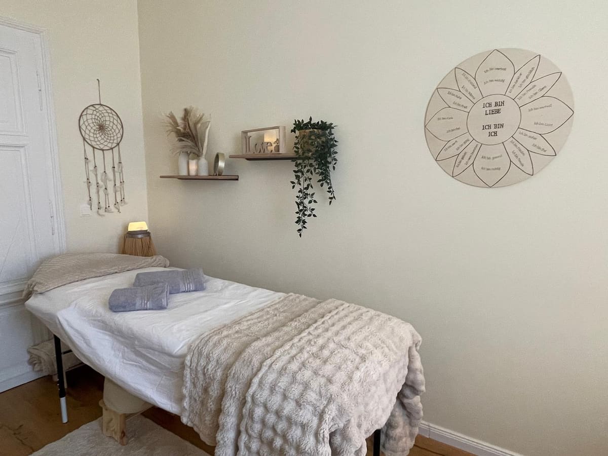 Behandlungsliege mit kuscheliger Decke und Affirmationsblume an der Wand